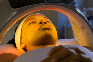 Woman receiving an LED facial treatment under a machine with a warm glow at Skin Devotee Facial Studio in Philadelphia
