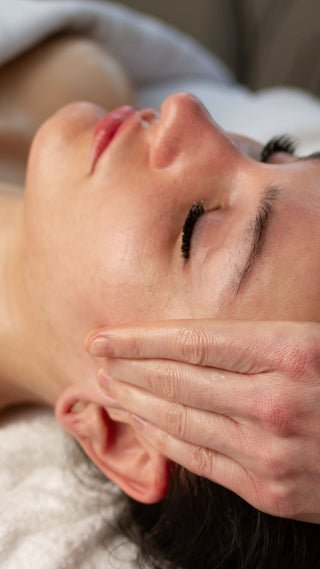 Young woman receiving a facial massage with hands applying pressure to her face at Skin Devotee Facial Studio in Philly
