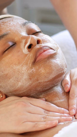 Young GenZ woman receiving a facial treatment with hands applying product to face at Skin Devotee Facial Studio