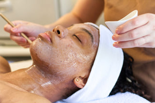 Person receiving a facial treatment with a skincare professional applying product at Skin Devotee Facial Studio in Philly.